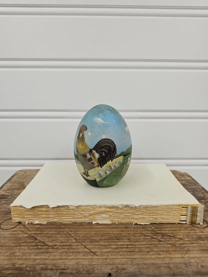 Small round painting of a landscape on a wooden surface with a white wall background