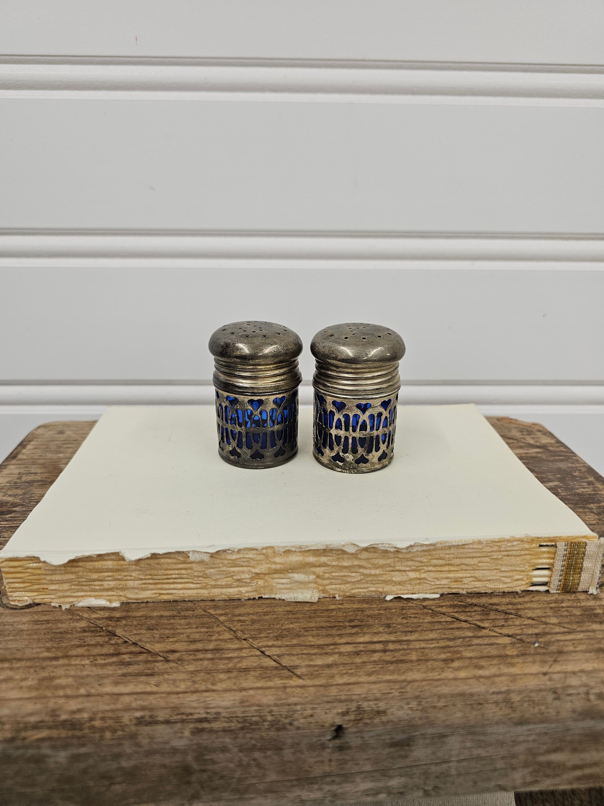 Two silver thimbles with blue patterns on a wooden surface next to a white cabinet.
