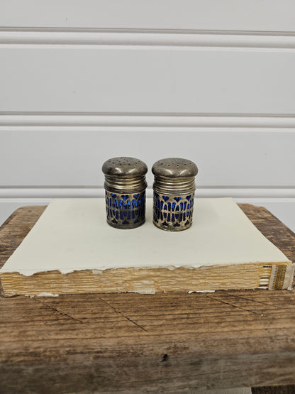 Two silver thimbles with blue patterns on a wooden surface next to a white cabinet.