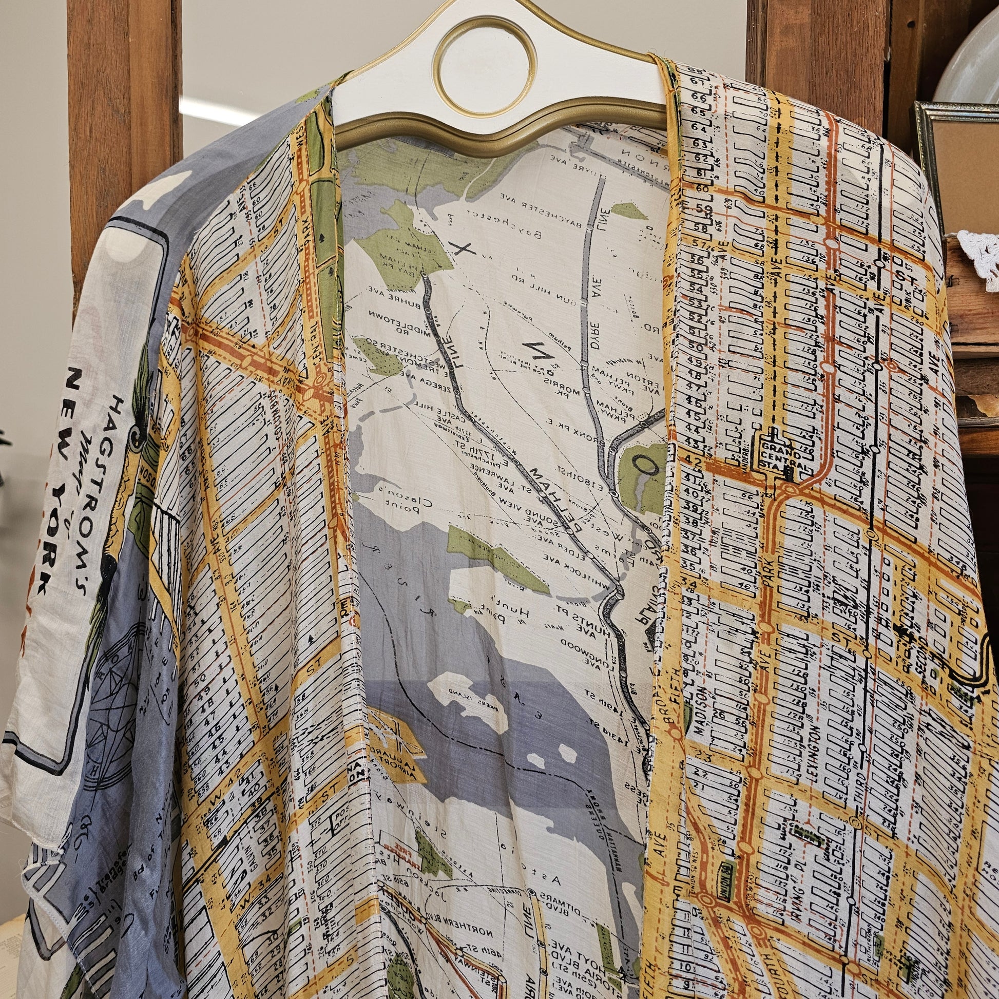 A lightweight open-front cardigan or kimono-style top with an all-over vintage city map print, hanging on a white hanger with a gold ring. The map design features New York City street lines and labels in muted yellow, gray, blue, and black tones.
