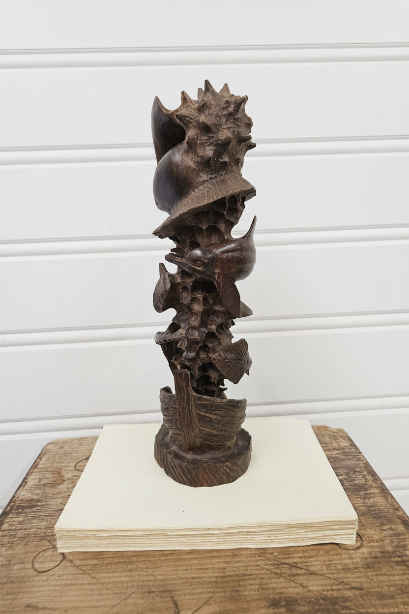 Decorative metal sculpture on a wooden stand against a white paneled wall.